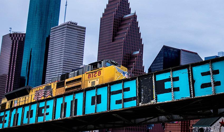 Picture of Houston buildings and train tracks with the painting "Be Someone".